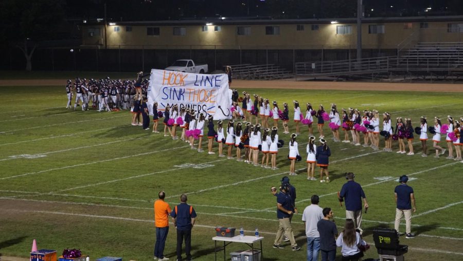 Cypress+cheer+team+and+song+team+hold+up+the+banner+for+the+Varsity+Football+team+to+run+through.