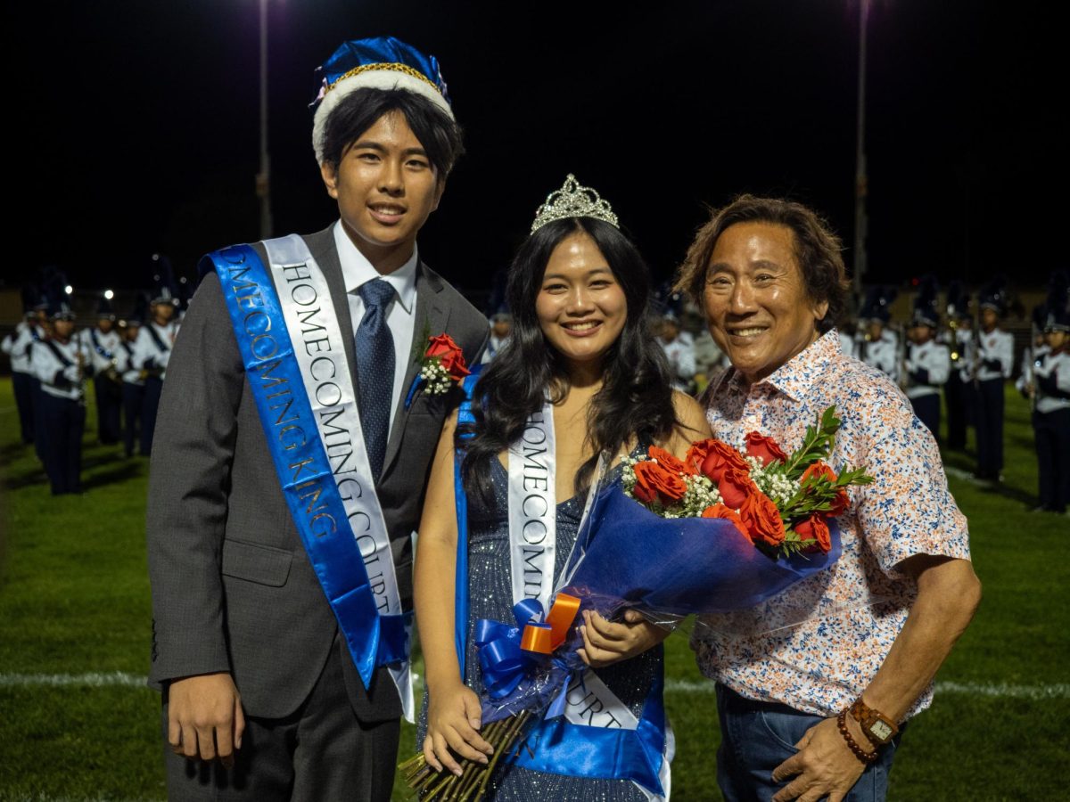 Homecoming King Josh Marinas and Homecoming Queen Jayda Juanillo standing beside Board of Trustees Member Mr. Hoshi moments after being crowned during the halftime show.